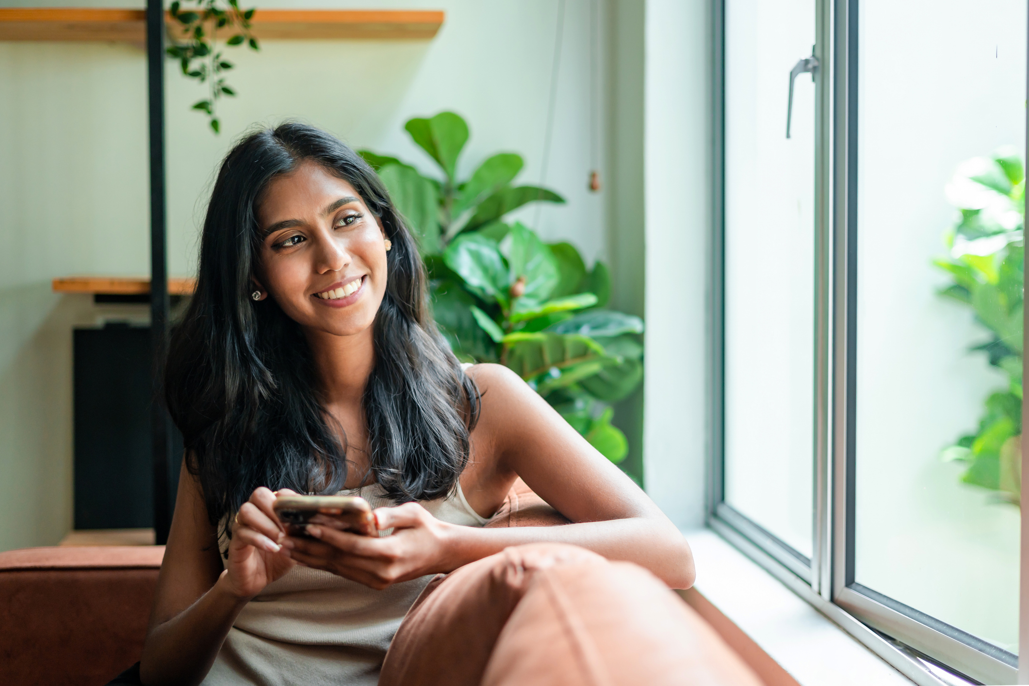 young woman sitting on sofa with cell phone at home