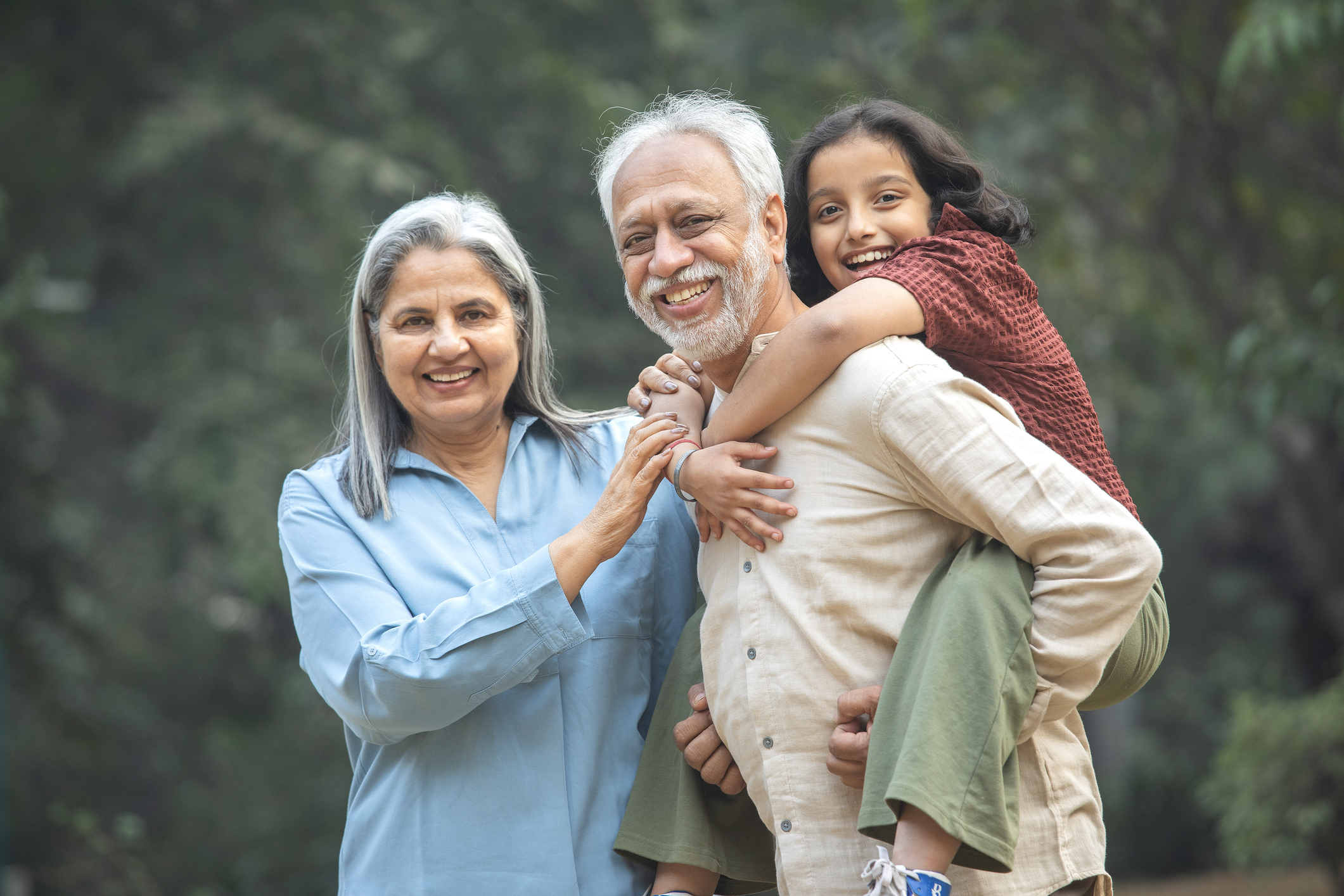 Smiling senior woman standing by senior man piggybacking playful granddaughter