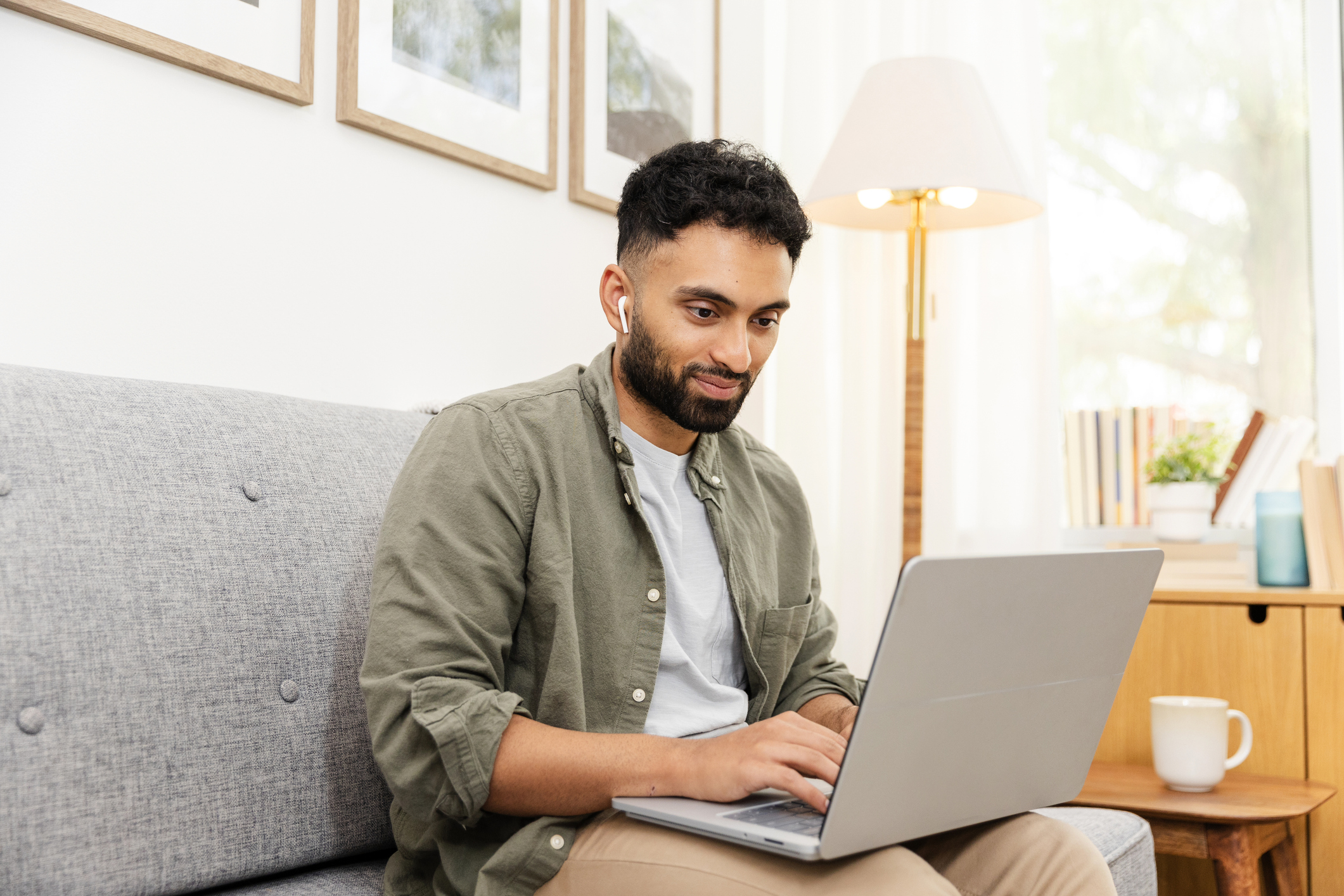 Young adult male student sits on the couch to type his paper