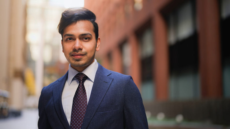 Portrait of handsome Indian businessman in city street A handsome Indian businessman in formal business suit is looking at the camera confidently and smiling happily in the city.
